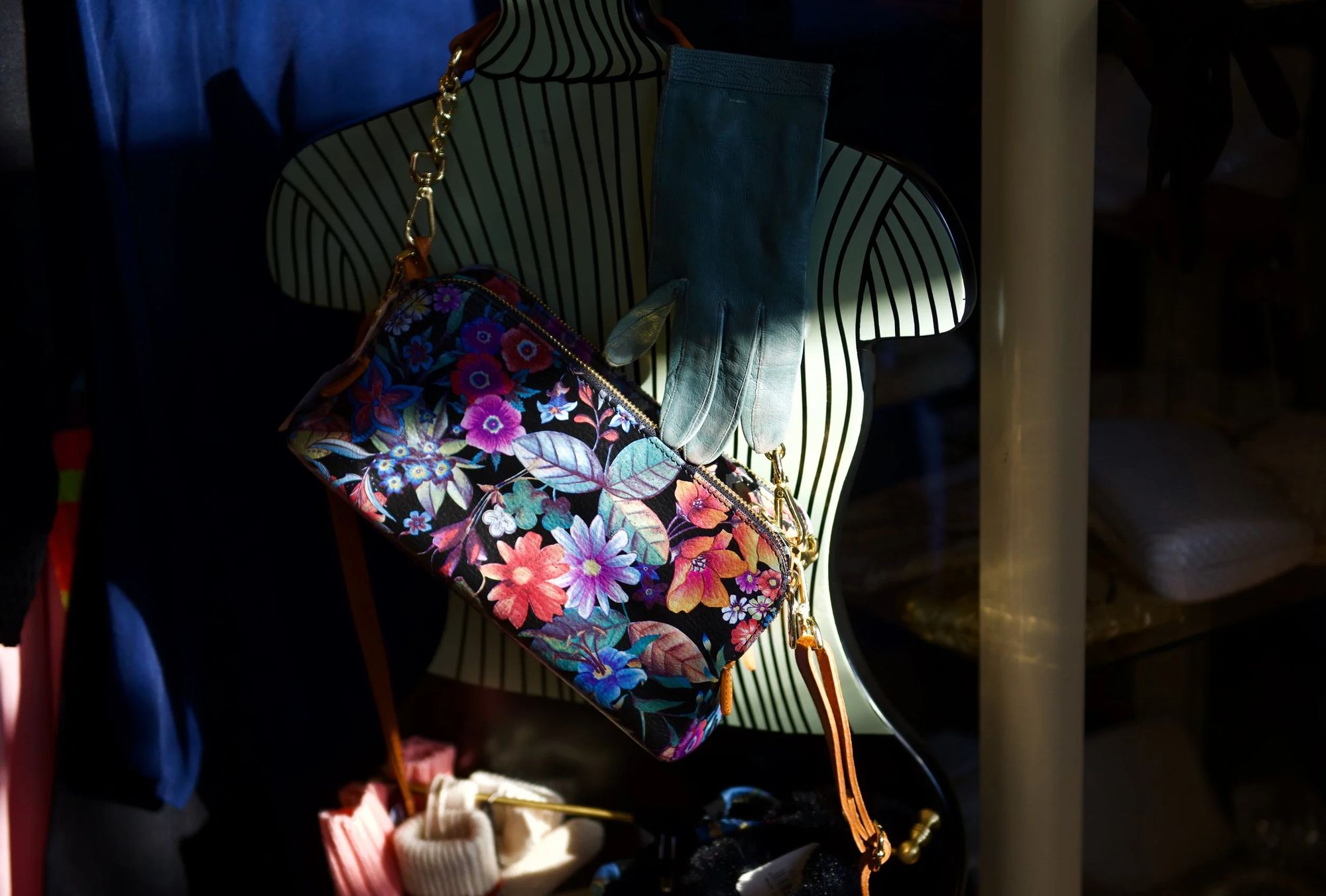 A floral print handbag and a pale blue leather glove on a striped dress form