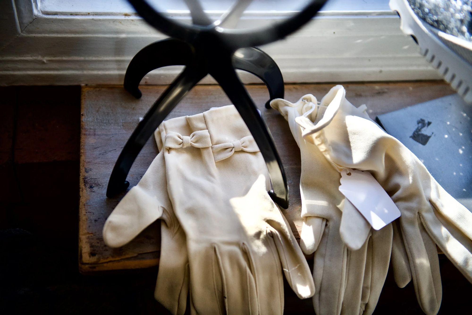 Two pairs of cream vintage gloves, one with bow detail, on a wooden sill